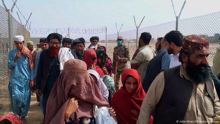 Crowds of people throng through a security barrier at the border between Afghanistan and Pakistan.