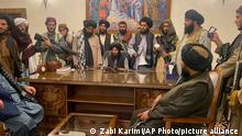 Taliban-Kämpfer mit Gewehren gruppieren sich stehend und sitzend um einen Schreibtisch im afghanischen Präsidentenpalast 