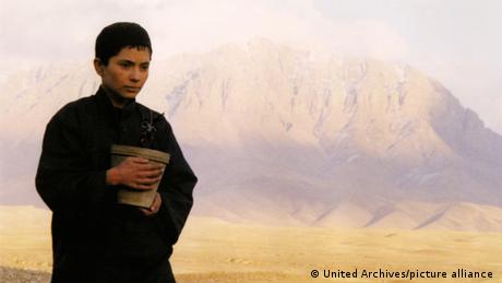 Film still from 'Osama' (2003) - a young person holding a bucket in a mountainous desert landscape.