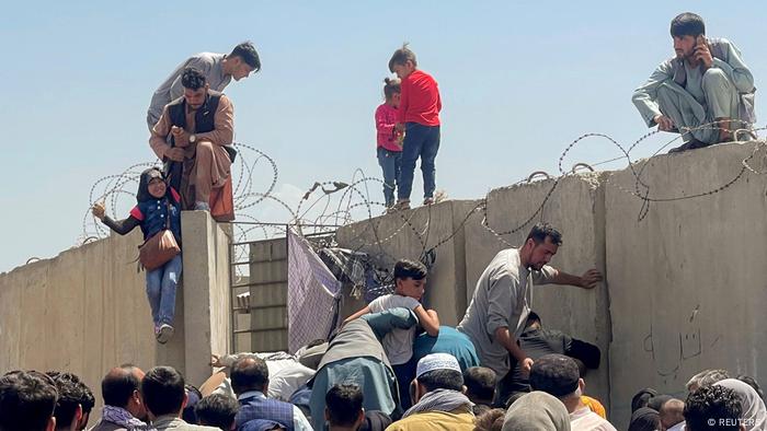 Children stand on top of a concrete wall as desperate crowds clamber into the Hamid Karzai International Airport precinct.