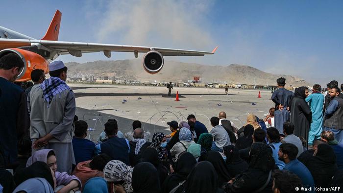 Afghan people sit on the tarmac of Kabul airport as they attempt to flee the Taliban rule of Afghanistan