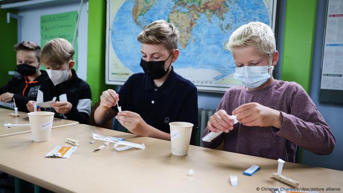 Children siting at desks with face masks, in the process of self-testing for COVID 