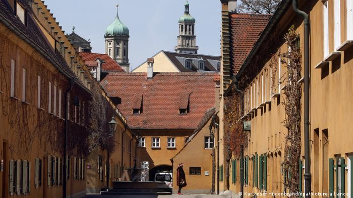 Shot of the alleys of the Fuggerei, with a view of the ochre-colored buildings and the old skyline of Augsburg in the background. The picture is from 2012.
