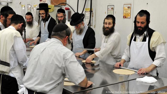 Orthodoxe Juden stehen gemeinsam in einer Küche und rollen Matzen aus.