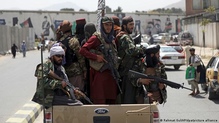 Taliban fighters hold their weapons as they drive around in the back of a pick up truck