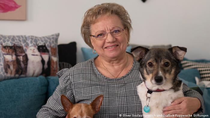 A woman smiles while holding her dogs on a sofa