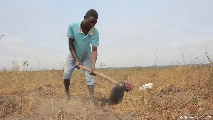 Ein Bauer in Angola bearbeitet einen vertrockneten Boden mit einer Hacke. 