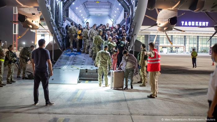 A group of refugees and military personnel in front of a plane