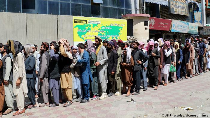 Afghans waiting in a line outside a bank to withdraw cash