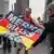 Участник акции протеста в Берлине держит флаг Германии с надписью "Меркель должна уйти"