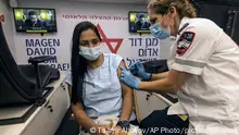 A medic from Israel's Magen David Adom emergency service administers a booster shot of the coronavirus vaccine to a woman in Tel Aviv, Israel, Saturday, Aug. 14, 2021. The country that had appeared to put the coronavirus pandemic behind it a few months ago after a world-leading vaccine drive is now re-imposing regulations in a bid to clamp back down on infections. (AP Photo/Tsafrir Abayov)