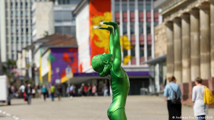 Eine grün glänzende Mädchenfigur steht in der Kasseler Fugängerzone und reckt die Arme in die Luft