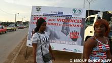 Two women walk by a banner denouncing the violence against women in Abidjan on August 31, 2021. (Photo by Issouf SANOGO / AFP)