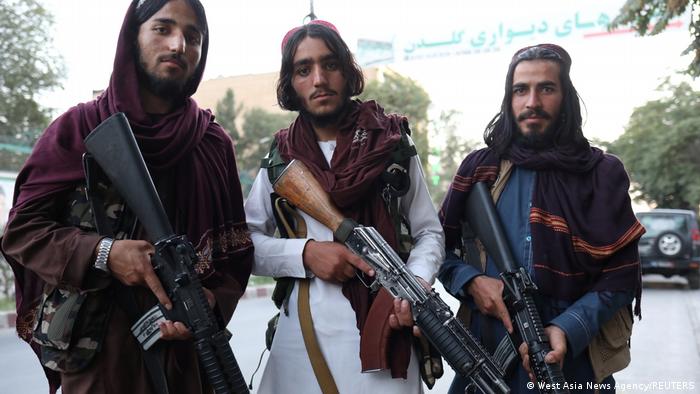Drei Taliban-Kämpfer mit Gewehren blicken in die Kamera