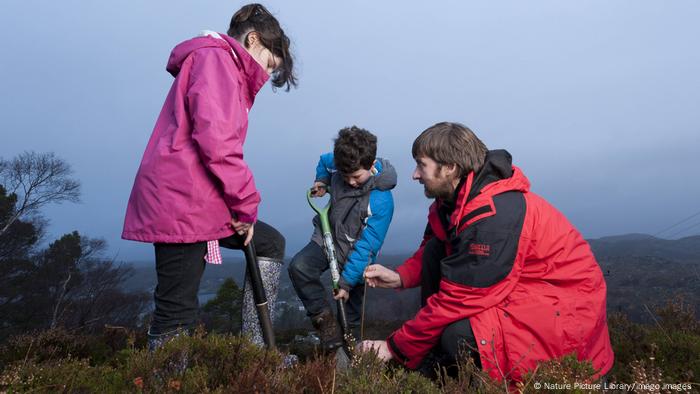 A man and two children plant trees in the Scottish Highlands