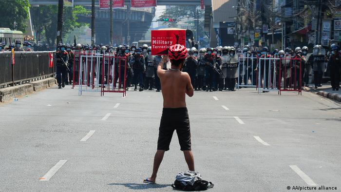Anti-coup protester shows placard to riot police as they protest against the military coup in Yangon, Myanmar