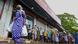 A woman carrying food bags walks pasts people standing in queue outside a state-run supermarket to buy essential food items in Colombo A woman carrying food bags walks pasts people standing in queue outside a state-run supermarket to buy essential food items in Colombo