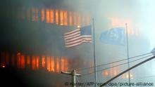 Vor einem der brennenden Zwillingstürme des World Trade Center in New York weht eine US-Nationalflagge am 11.9.2001. Zwei Flugzeuge sind an diesem Morgen kurz hintereinander in die Türme des World Trade Center gerast. Bei den schweren Explosionen wurden wahrscheinlich außer den Insassen der Maschinen zahlreiche Menschen innerhalb der beiden Wolkenkratzer getötet. Das FBI geht dem Verdacht nach, dass es sich um einen gezielten Anschlag von terroristischen Selbstmord-Attentätern handelt. Die oberen Teil der Wolkenkratzer gingen nach Explosionen in Flammen auf. Wrack- und Gebäudeteile der 411 Meter hohen Zwillingstürme flogen auf die Straße.