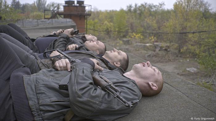 Four men in dark clothing with weapons lay on the ground.