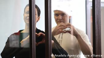 Мария Колесникова и Максим Знак в зале суда показывают руками сердечки
