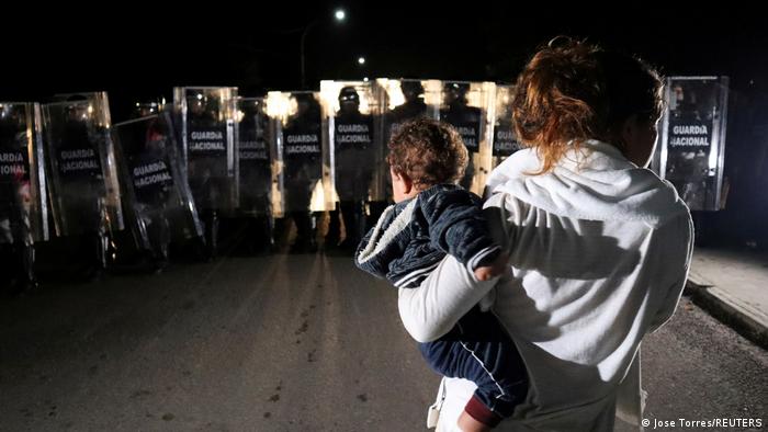 Foto de una persona con un bebé en manos frente a agentes de la Guardia Nacional de México.