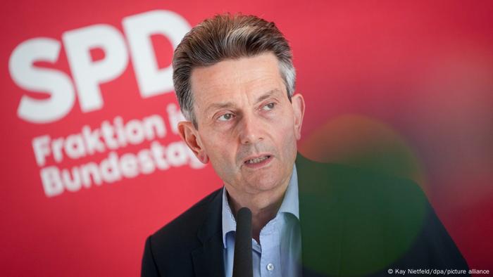 Rolf Mützenich steht vor einer roten Wand vor dem Fraktionssaal der SPD im Bundestag und redet