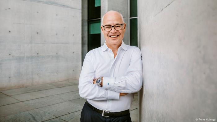 Sven Gösmann in a white shirt with crossed arms in front of grey cement walls