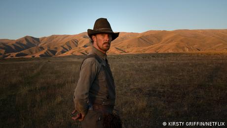 Benedict Cumberbatch in a cowboy hat standing on the plains of Montana with mountains in the background