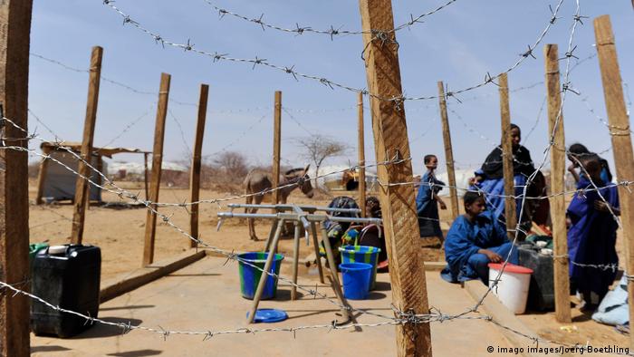 People sit behind a barbed wire fence in a refugee camp