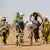 Des femmes et des enfants vus de dos qui partent dans le désert, très chargés (illustration)