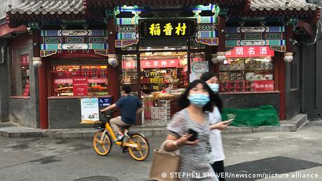 Very few Chinese, all wearing masks outdoors, walk through a normally busy historic neighborhood in Beijing