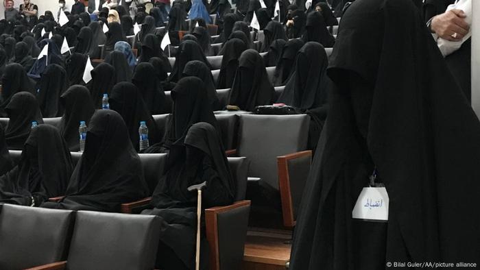 Ein Hörsaal, auf den Stühlen sitzen schwarz gekleidete voll verschleierte Frauen, einige von ihnen tragen kleine Fähnchen