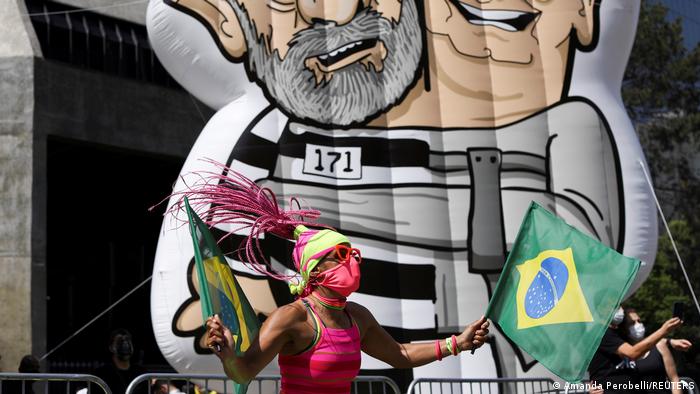 Ein Demonstrant mit zwei brasilianischen Flaggen vor eine großen aufblasbaren zweiköpfigen Puppe, die Präsident Bolsonaro und den Ex-Präsidenten Lula da Silva darstellt
