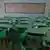 An empty classroom full of green desks and chairs