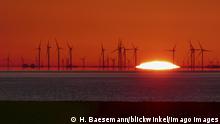 A series of wind turbines backed by the rising orange sun