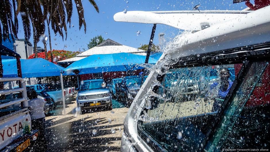 Storefronts, buildings, a car wash, a car dealership and pedestrians sprayed with water