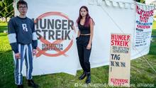 Two young activists stand in front of the hunger strike banners and tents