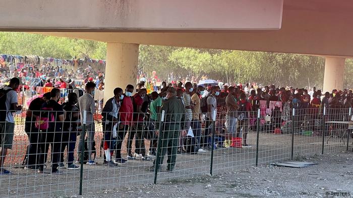 Imigrantes em pé fazem fila sob ponte