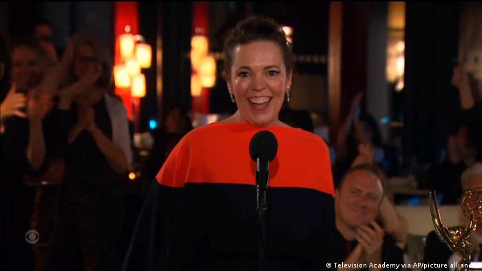 Olivia Colman freut sich bei den Emmys über ihren Preis. Sie steht an einem Mikrofon, hinter ihr klatschen sitzende Menschen.