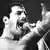 Freddie Mercury in 1984, man sings into microphone and gesticulates.