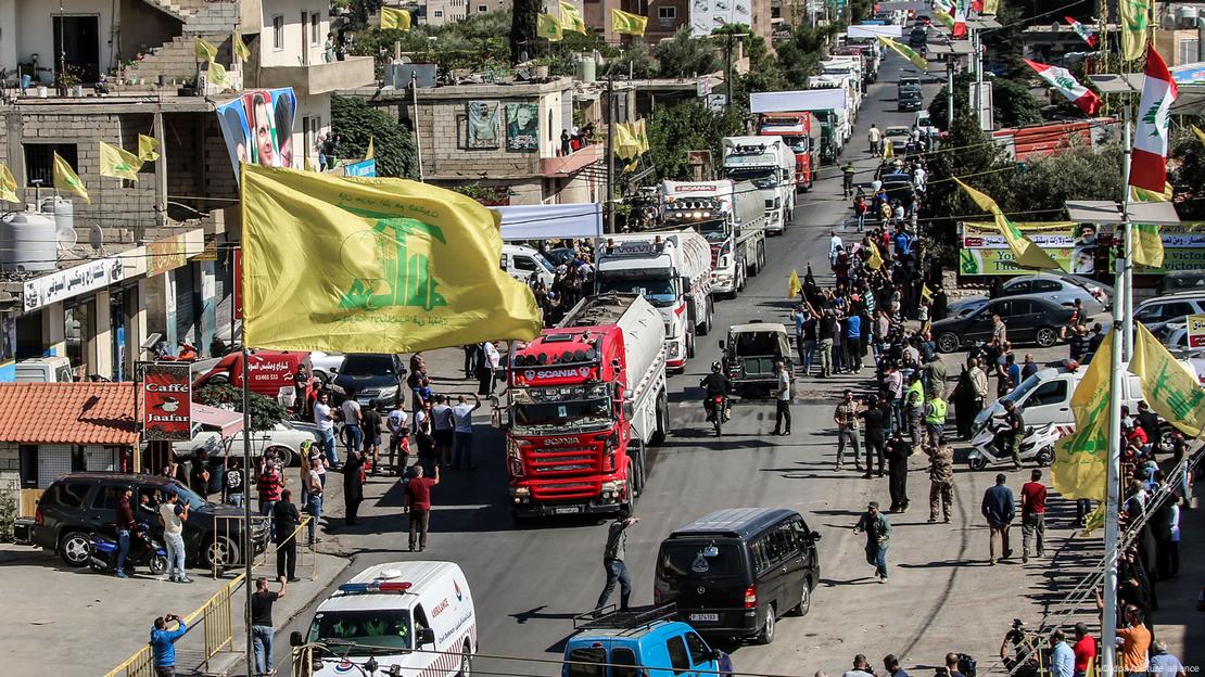 Kamionë cisterna hyjnë në fshatin lindor libanez të al-Ayn, rrugë e qytetit me flamuj të verdhë, njerëz në rrugë pranë kamionëve Kamionë cisterna hyjnë në fshatin lindor libanez të al-Ayn, rrugë e qytetit me flamuj të verdhë, njerëz në rrugë pranë kamionëve