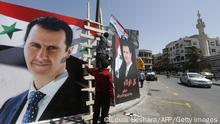 Men hang the national flag next to posters of President Bashar al-Assad, a candidate for the Presidential election, in the Syrian capital Damascus on May 17, 2021. - A Syrian former minister and a member of the Damascus-tolerated opposition will face Bashar al-Assad in this month's presidential election, the constitutional court said. The Assad-appointed body approved only three out of 51 applications to stand in the May 26 ballot, among them the 55-year-old president himself, widely expected to win a fourth mandate. (Photo by LOUAI BESHARA / AFP) (Photo by LOUAI BESHARA/AFP via Getty Images)