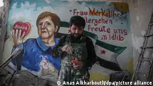 Aziz Al-Asmar, ein syrischer Maler aus Binnish, steht vor seinem Wandgemälde in einem beschädigten Gebäude, das die deutsche Bundeskanzlerin Angela Merkel darstellt. Darauf ist auch die Aufschrift «Frau Merkel Ihr Wohlergehen freute uns in Idilib» zu lesen. Merkel hatte sich am Sonntagabend (22.03.2020) in häusliche Quarantäne begeben, nachdem sie darüber unterrichtet worden war, dass sie am Freitag (20.03.2020) zu einem Arzt Kontakt hatte, der mittlerweile positiv auf das Coronavirus getestet wurde. Bei einem zweiten Test auf das neuartige Coronavirus sei bei Merkel keine Infektion festgestellt worden, teilte ein Regierungssprecher am Mittwoch (25.03.2020) in Berlin mit.