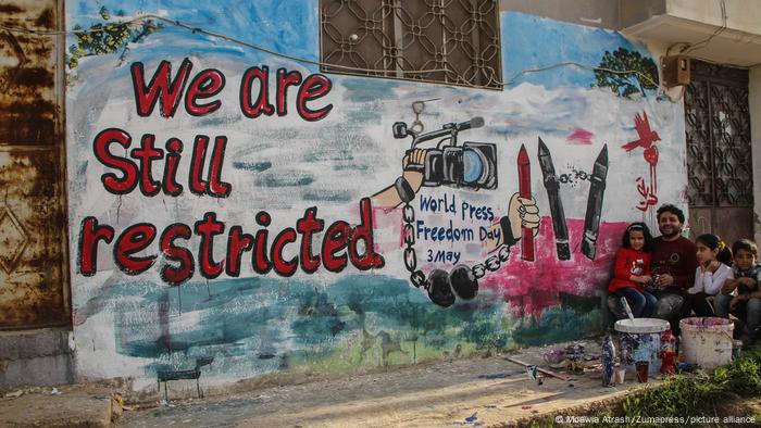 Man paints a mural on a wall with the words We are still restricted.