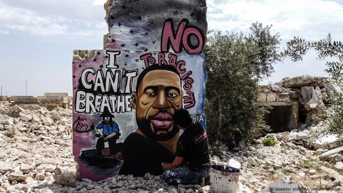 A man paints a portrait of a Black man on a wall that stands amid rubble.