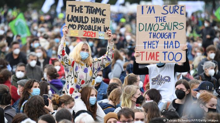 A participant holds a sign reading The Titanic would have no problem in 2021 during a Fridays for Future global climate strike in Berlin, while another holds a sign reading: I'm sure the dinosaurs thought they had time too