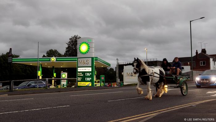 A horse-drawn wagon passes a gas station in the UK.