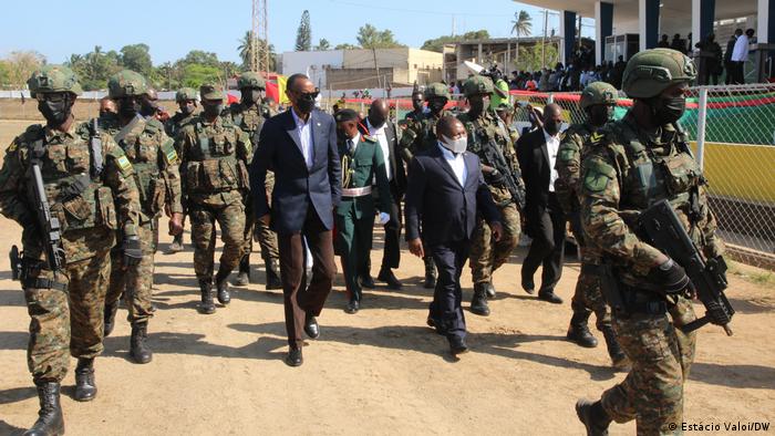 Kagame und Nyusi gehen auf einem sandigen Weg umringt von schwerbewaffneten Soldaten