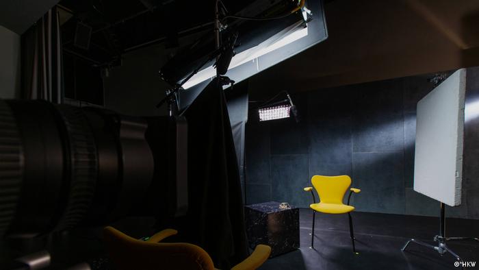 Ein gelber Stuhl steht in einem leeren, dunklem Raum und wird beleuchtet.