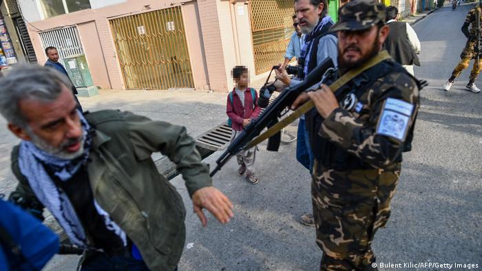 A member of the Taliban special forces pushes a journalist (L) covering a demonstration by women protestors outside a school in Kabul